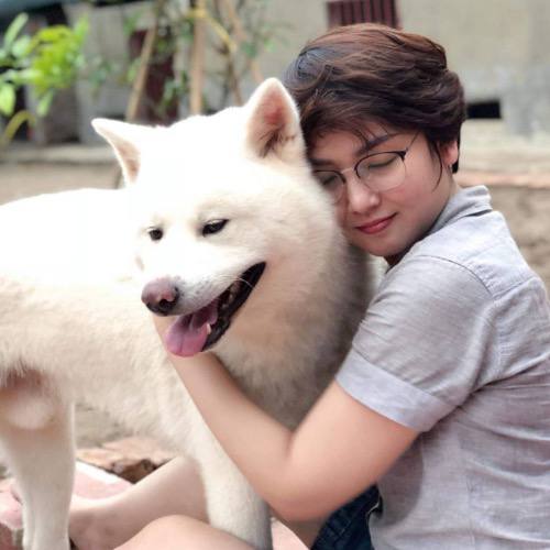 Người phụ nữ ôm chó Akita Inu trắng trong khung cảnh ấm áp.