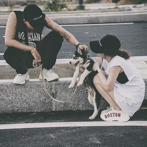 Hai bạn trẻ đội mũ đen dắt chó Husky đen trắng đi dạo ngoài trời