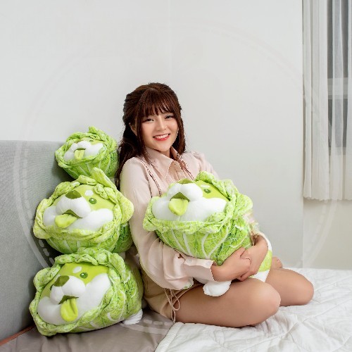 Gấu bông chó Shiba bắp cải đáng yêu với thiết kế độc đáo, được cô gái ôm trên giường.